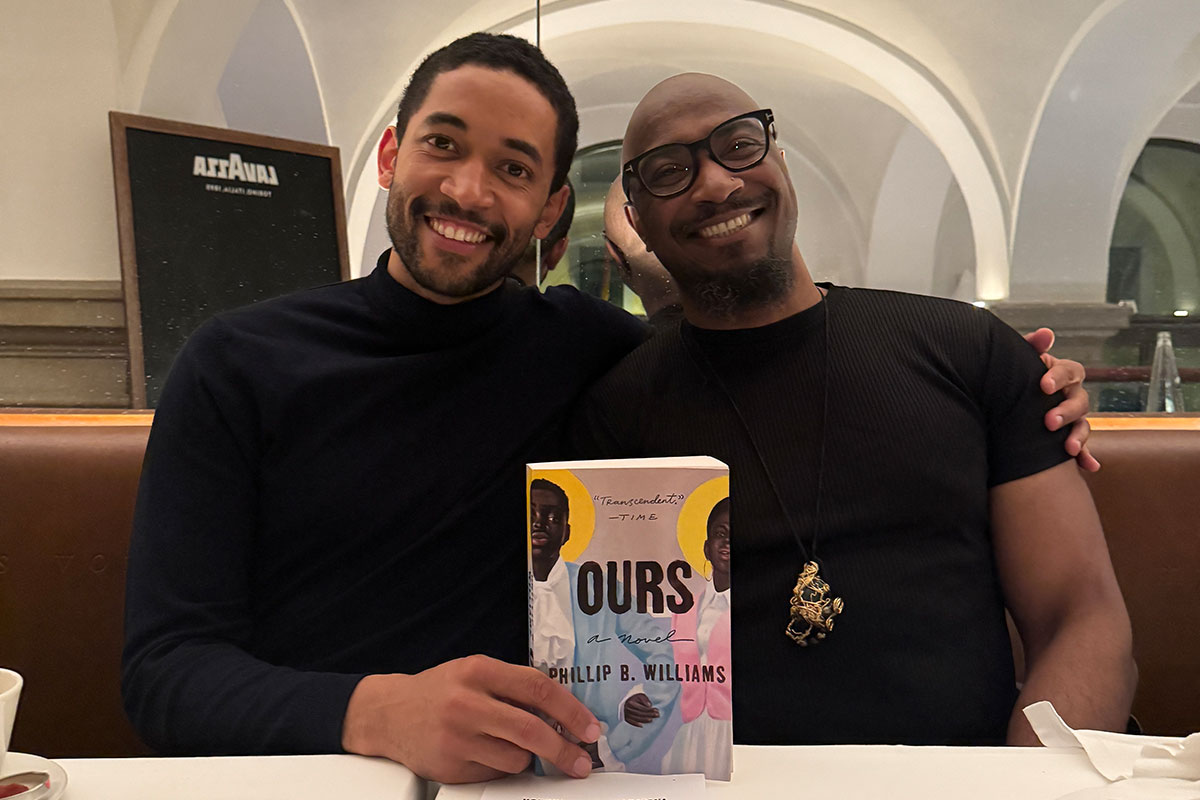 Schauspieler Benito Bause sitzt im Kaffeehaus neben Autor Phillip B. Williams mit dessen Buch OURS in der Hand